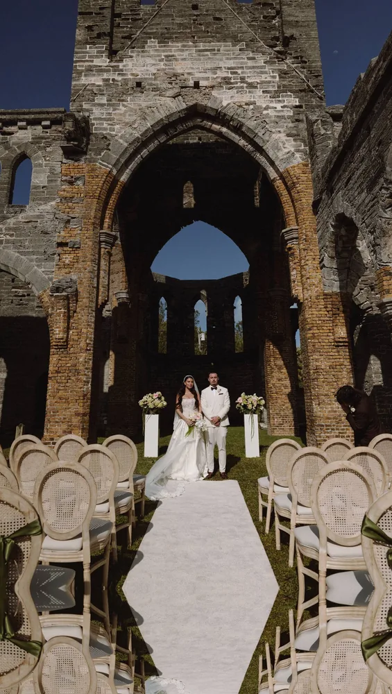 Bride walking the aisle of a roofless stone church, open to the sky